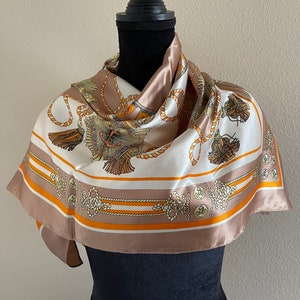 May include: A white silk scarf with a brown and orange pattern of nautical ropes and anchors. The scarf is draped around a black mannequin.