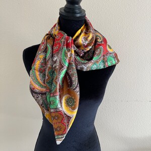 Pu&ograve; includere: Sciarpa paisley multicolore, esposta su un manichino nero. I colori includono rosso, verde, giallo e marrone. Il tessuto sembra essere seta o simile, con una leggera lucentezza.