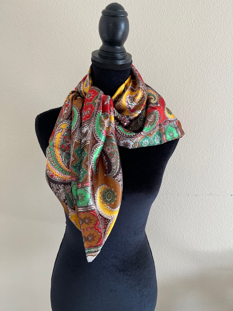 Pu&ograve; includere: Sciarpa paisley multicolore, esposta su un manichino nero. I colori includono rosso, verde, giallo e marrone. Il tessuto sembra essere seta o simile, con una leggera lucentezza.