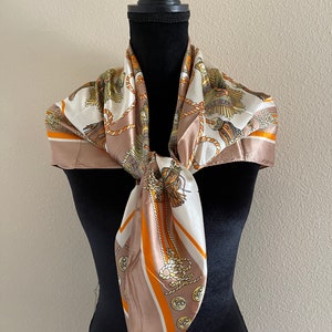 May include: A brown and white silk scarf with a pattern of gold ropes and buttons. The scarf is tied around a black mannequin's neck.
