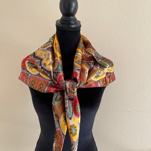 Pu&ograve; includere: Una sciarpa paisley colorata nei toni del giallo, rosso, marrone e verde &egrave; drappeggiata attorno a un manichino nero. La sciarpa &egrave; annodata sul davanti, mostrando il suo motivo intricato e i colori vivaci. Questo accessorio aggiunge un tocco vintage.
