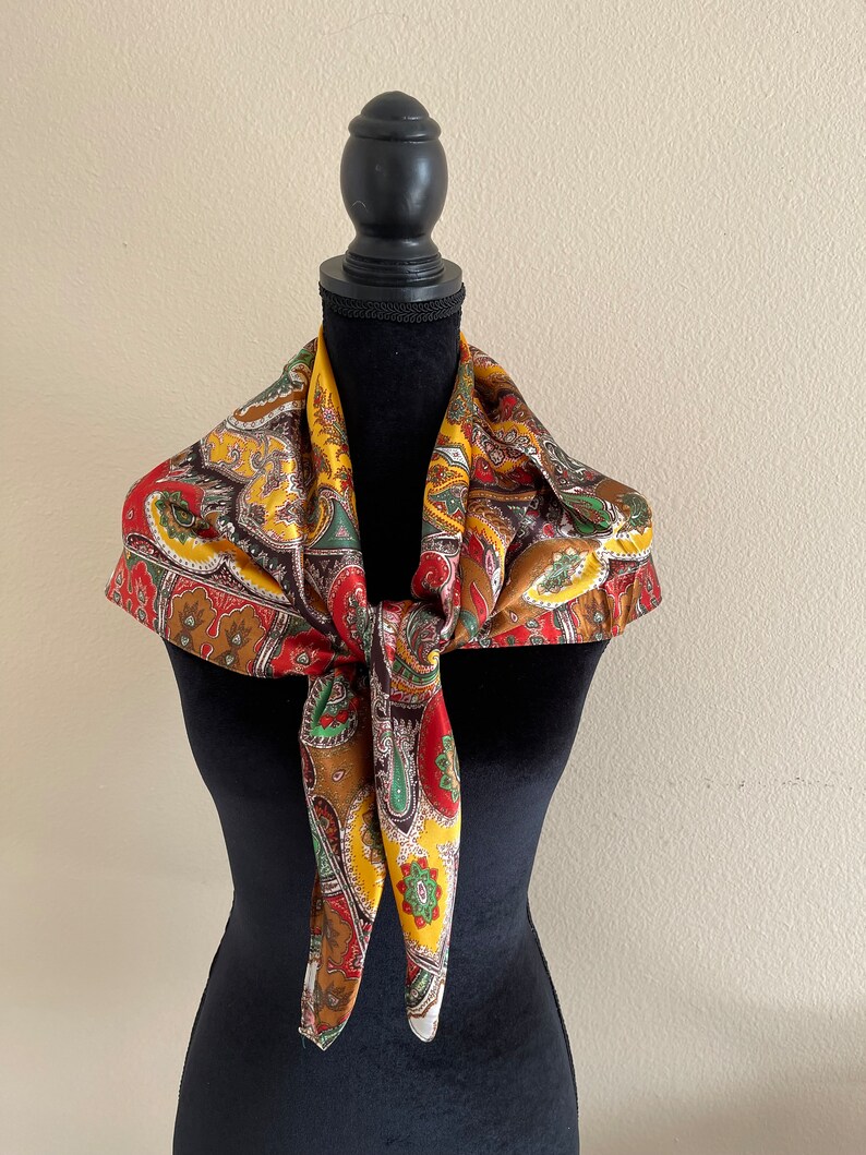 Pu&ograve; includere: Una sciarpa paisley colorata nei toni del giallo, rosso, marrone e verde &egrave; drappeggiata attorno a un manichino nero. La sciarpa &egrave; annodata sul davanti, mostrando il suo motivo intricato e i colori vivaci. Questo accessorio aggiunge un tocco vintage.