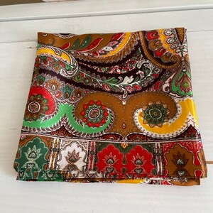 Pu&ograve; includere: Tessuto piegato con motivo paisley nei toni del marrone, giallo, rosso e verde. Il tessuto presenta un design dettagliato con motivi floreali e a goccia. Il tessuto &egrave; piegato ordinatamente, mostrando l'intricato motivo.