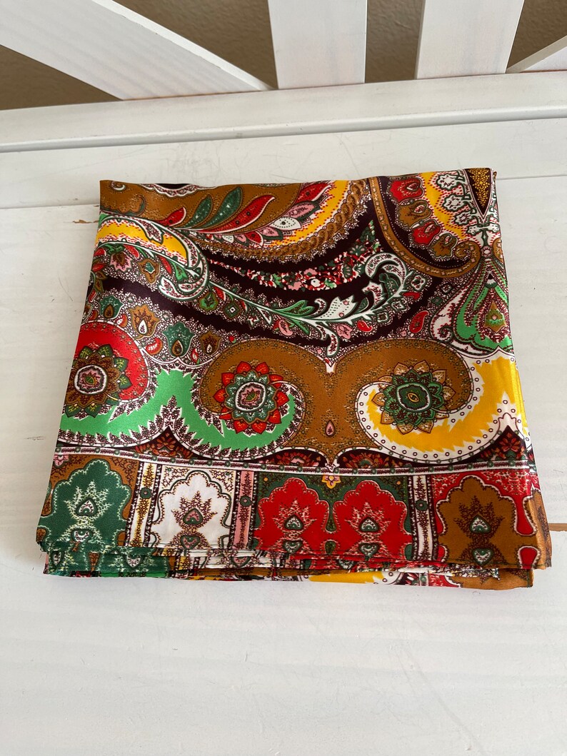 Pu&ograve; includere: Tessuto piegato con motivo paisley nei toni del marrone, giallo, rosso e verde. Il tessuto presenta un design dettagliato con motivi floreali e a goccia. Il tessuto &egrave; piegato ordinatamente, mostrando l'intricato motivo.