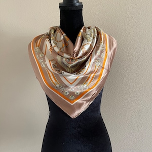 May include: A brown silk scarf with a white and gold pattern of ropes and knots. The scarf is on a black mannequin.