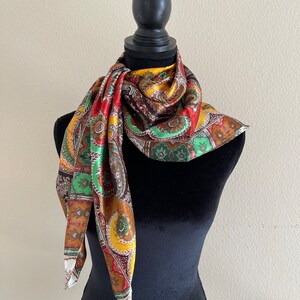 Pu&ograve; includere: Una sciarpa colorata con motivo paisley nei toni del rosso, verde, giallo e marrone &egrave; drappeggiata su un manichino nero. La sciarpa ha una lucentezza setosa e un design dettagliato. La sciarpa quadrata &egrave; piegata e annodata intorno al collo del manichino.