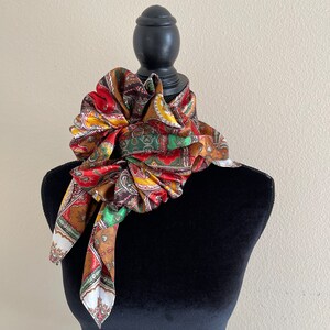 Pu&ograve; includere: Una sciarpa paisley colorata, nei toni del rosso, marrone, giallo, verde e bianco, &egrave; drappeggiata attorno a un manichino nero. La sciarpa &egrave; annodata e disposta per mostrare il suo motivo intricato e i colori vivaci, creando un accessorio decorativo.