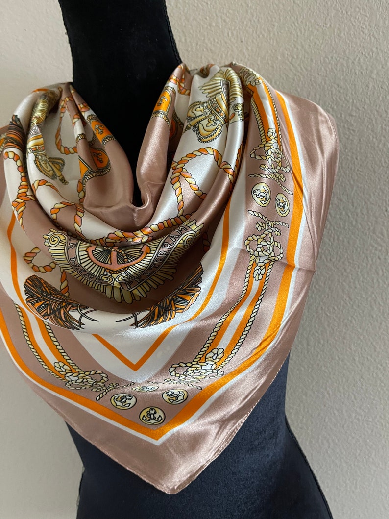 May include: A brown silk scarf with a white and orange pattern of nautical rope, anchors, and crests.