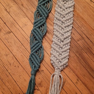 Op de afbeelding: Twee handgemaakte macramé-bladwijzers, één in teal en één in grijs, met kwastjes aan de onderkant.