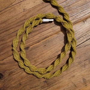 Op de afbeelding: Een groene gevlochten oplaadkabel met witte connectoren. De kabel is opgerold tot een cirkel en ligt op een houten oppervlak.