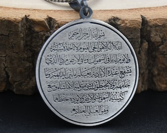 Può includere: Una collana d'argento con un ciondolo rotondo con calligrafia araba. Il ciondolo è inciso con il testo "بسم الله الرحمن الرحيم" e altri versi del Corano.
