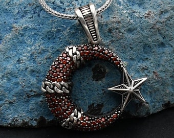 Può includere: Una collana con catena d'argento con un ciondolo a forma di mezzaluna e stella. Il ciondolo è incrostato di pietre preziose rosse.