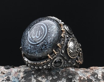 Può includere: Un anello d'argento con una pietra nera che presenta calligrafia araba, inclusa la parola "Allah". L'anello è decorato con dettagli intricati e pietre nere e bianche.
