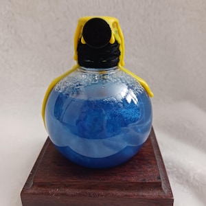 Puede incluir: Un orbe de vidrio azul con un sello de cera amarilla en la parte superior, sentado sobre una base de madera oscura.