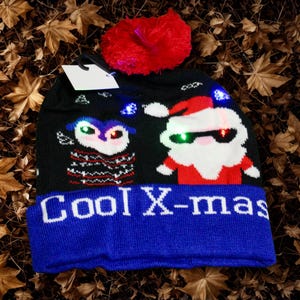 May include: Black knitted Christmas hat with a red pom-pom and blue brim. The hat features an owl and Santa Claus design with LED lights and the text "Cool X-mas".