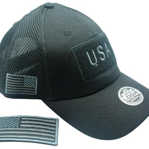 May include: Black mesh and cotton baseball cap with a black USA patch and a black and gray American flag patch. The cap has a black adjustable strap with a black logo.
