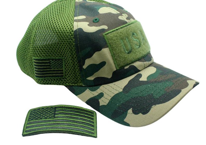 May include: A green camouflage baseball cap with a mesh back panel. The cap has a green velcro patch with the text "U.S.A." embroidered on it. The cap also has a small green and black American flag patch on the side. A separate green and black American flag patch is also included.