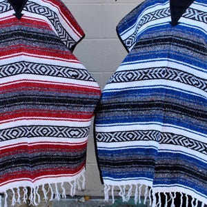 May include: Two colorful Mexican ponchos with fringe. One poncho is red, white, and black, and the other is blue, white, and black.