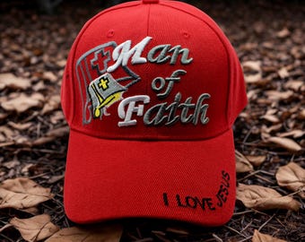 May include: A red baseball cap with the embroidered text "Man of Faith" in white and gray. The cap also features a cross and a bible design. The phrase "I Love Jesus" is embroidered on the brim.