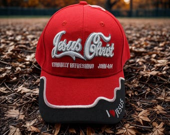 May include: A red baseball cap with the words "Jesus Christ" embroidered in white script. The cap also features the text "Eternally Refreshing John 4:14" and "I ❤️ Jesus" on the brim. The brim is black with a white wavy design.