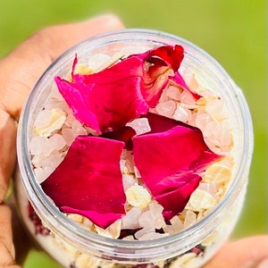 May include: A clear glass jar filled with bath salts, oatmeal, and dried rose petals. The petals are a vibrant pink color.