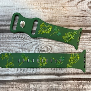 May include: Two green Apple Watch bands featuring a frog and dragonfly design. The bands are made of silicone and have a green and yellow colour scheme.