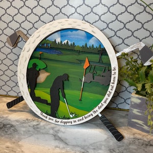 Puede incluir: Una bola de golf de madera blanca con una escena de campo de golf verde en su interior. La bola de golf est&aacute; rodeada por dos palos de golf negros con empu&ntilde;aduras blancas. El texto "Thank you for stepping in and being the dad you did not have to be." est&aacute; escrito alrededor del borde de la bola de golf.