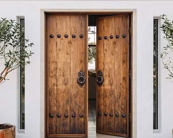 Pode incluir: Um par de portas duplas de madeira rústica com tábuas verticais, aldravas circulares de metal escuro e filas de tachas decorativas pretas. As portas estão inseridas numa parede branca com telhado curvo, ladeadas por duas árvores em vasos de terracota.