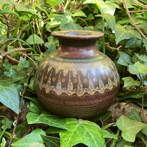 以下が含まれることがあります： 緑、茶色、オレンジの色合いで幾何学模様が施された茶色の陶器の花瓶。花瓶は丸みを帯びたボディとわずかに広がった開口部を持っています。