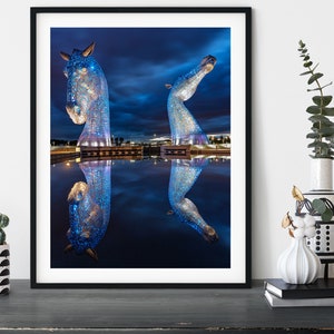 Large blue horse head sculptures in Scotland with water reflection at night.