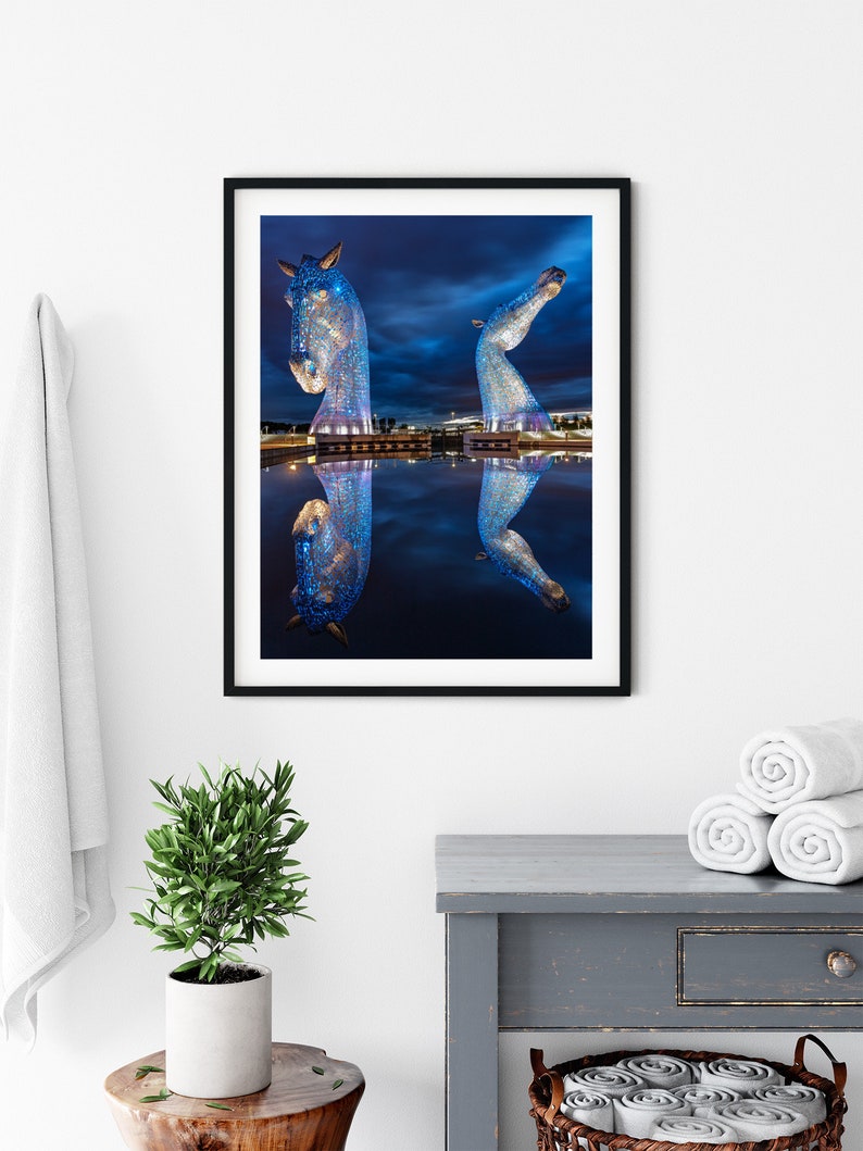 Large blue horse head sculptures in Scotland with water reflection at night.