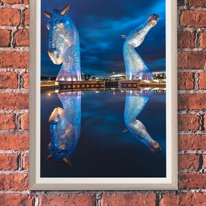 May include: Two blue, metallic horse sculptures stand in a body of water, reflecting the night sky. The sculptures are illuminated with blue lights, creating a vibrant and modern art piece.