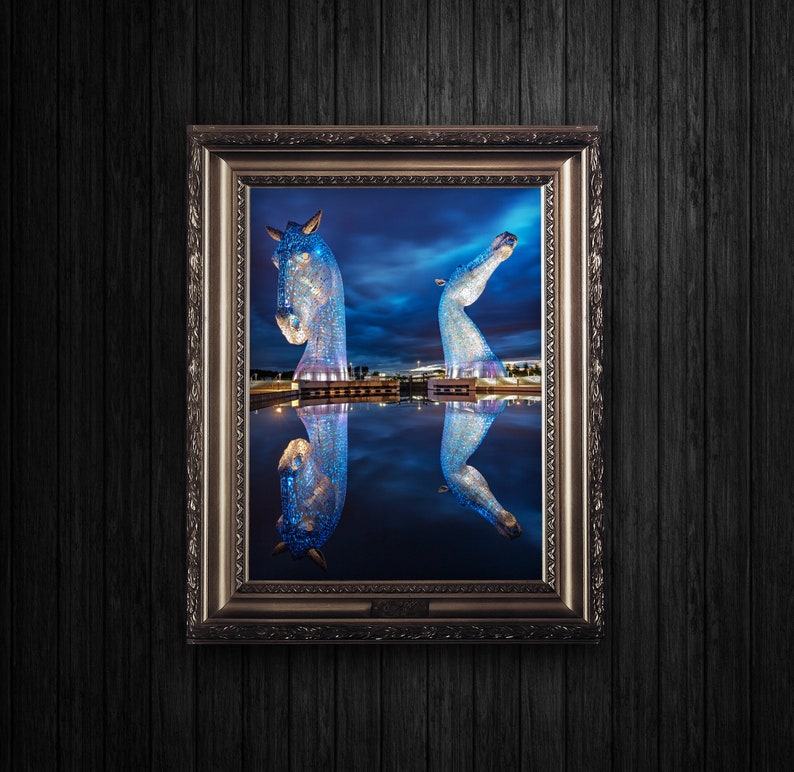 May include: A framed photograph of a blue, illuminated sculpture of two horses, reflected in a still body of water at night. The sculpture is made of many small, reflective pieces, creating a shimmering effect.