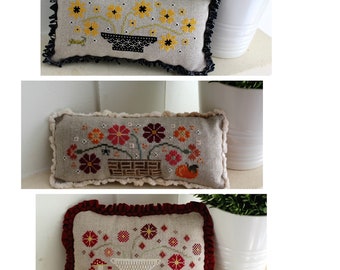 May include: Three embroidered cushion covers featuring floral designs. The first cushion has a yellow and black floral design with a black pot. The second cushion has a red, orange, and green floral design with a brown basket. The third cushion has a red and white floral design with a white bowl.