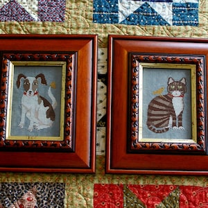 May include: Two framed cross-stitch pieces, one with a dog and the other with a cat. Both are in brown frames with gold trim and feature a small bird on the side.