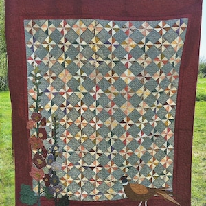 May include: Handmade quilt with a geometric pattern in shades of gray, blue, and various colors. The quilt features a burgundy border and appliqued flowers and a pheasant. A unique, handcrafted textile for home decor.