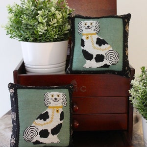 Könnte beinhalten: Zwei dekorative Kissen mit grünem Hintergrund und einem schwarzen und weißen Hundemuster. Die Kissen liegen auf einer Holzkiste mit Schubladen. Die Kiste ist geöffnet und die Schublade ist herausgezogen.