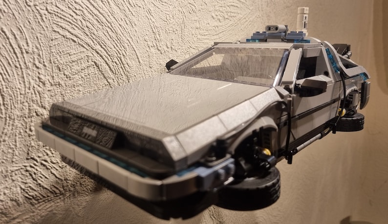 May include: A white and gray Lego model of the DeLorean time machine from the Back to the Future movie. The car is hovering in the air with its wheels extended.