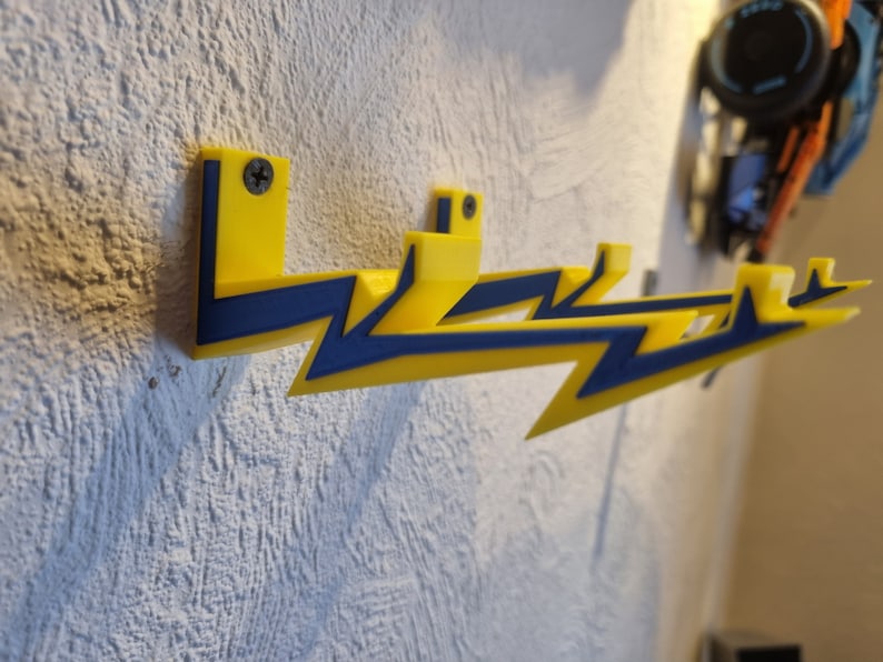 May include: Three yellow lightning bolt shaped wall hooks with blue accents. The hooks are mounted on a white wall.