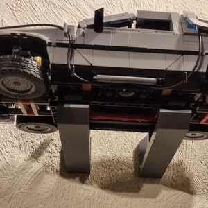May include: A gray and black Lego model of the DeLorean time machine from the Back to the Future movie series. The model is mounted on a wall-mounted stand.