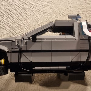 May include: A gray Lego model of the DeLorean time machine from the Back to the Future movie series. The model has a detailed interior and exterior, including the iconic flux capacitor and gull-wing doors.