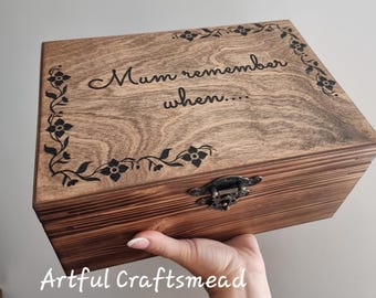May include: A wooden memory box with the words "Mum remember when..." engraved on the lid. The box is stained a warm brown and features floral corner accents. A metal clasp secures the box. The text "Artful Craftsmead" is at the bottom.