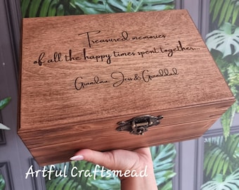 May include: A wooden keepsake box with a hinged lid and metal clasp. The box is engraved with the words "Treasured memories of all the happy times spent together... Grandma, Jen & Granddad." The box is held in a hand.