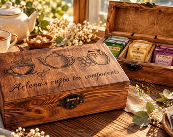 May include: A rectangular wooden tea storage box with a hinged lid and metal latch. The lid features an engraved illustration of a teacup, teapot, and honey jar, with the text Arlena's cuppa tea components. The open box contains tea bags.