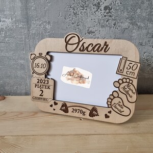 Könnte beinhalten: Holzbildrahmen mit einer personalisierten Inschrift "Oscar" und Details wie einer Uhr, einem Datum, einem Gewicht und Fußabdrücken. Der Rahmen ist mit Herzen und einer Hantel verziert.