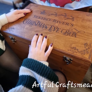 May include: A wooden Christmas Eve box with the text "SEKIRO-RIVER'S CHRISTMAS EVE BOX" engraved on the lid. The box is rectangular, with metal clasps and decorative corner designs. The box is a warm brown color.