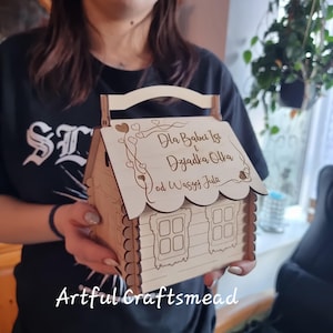 May include: A wooden house-shaped box with a handle, decorated with hearts and vines. The box has a sign that reads "Dla Babci Iza i Dziadka Olka od Waszej Juli".