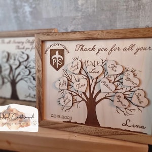 以下が含まれることがあります： 木製のプレートに木とハートが描かれており、ハートには「愛」「楽しみ」「サポート」「時間」などの言葉が書かれています。プレートは木製のフレームで囲まれており、「あなたのすべてに感謝を込めて...」と「レナ」の文字が書かれています。プレートには「Eton Porny School」と「2019-2023」の文字も書かれています。