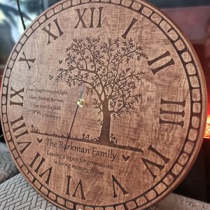 Könnte beinhalten: Eine runde Holzuhr mit römischen Ziffern und einem Baumdesign. Das Zifferblatt zeigt den Text "The Barkman Family" und ein Zitat aus 2. Timotheus 4:7. Die Uhrzeiger sind goldfarben.