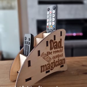 May include: Wooden remote control holder with the text "Dad, the remote control magician" engraved on it. The holder has slots for multiple remotes.